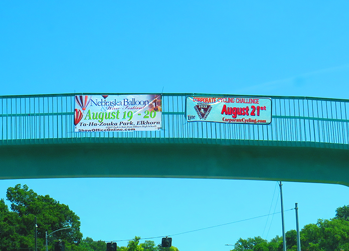 Two signs hang off of the bridge by UNO's main campus, text is below